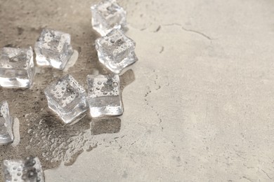 Melting ice cubes and water drops on grey textured table, closeup. Space for text