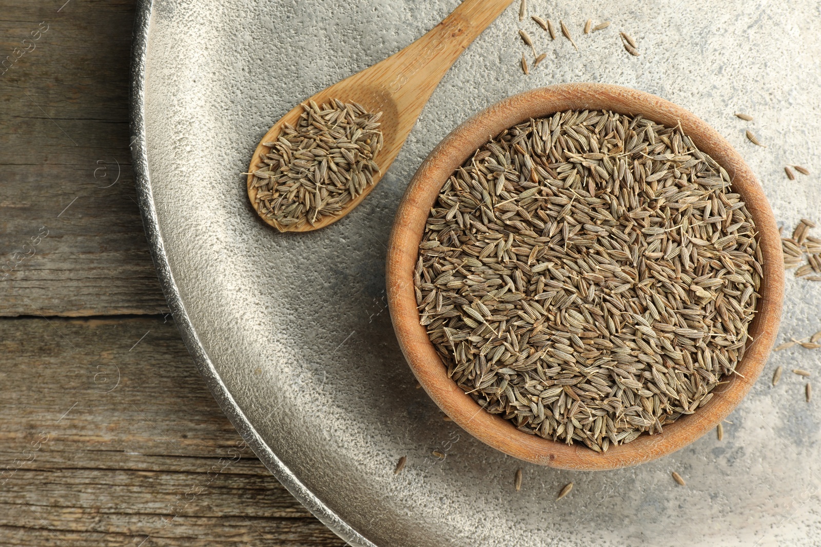 Photo of Bowl of caraway seeds and spoon on wooden table, top view