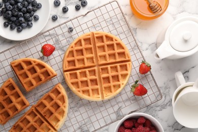 Photo of Tasty Belgian waffles with fresh berries and honey on white marble table, flat lay