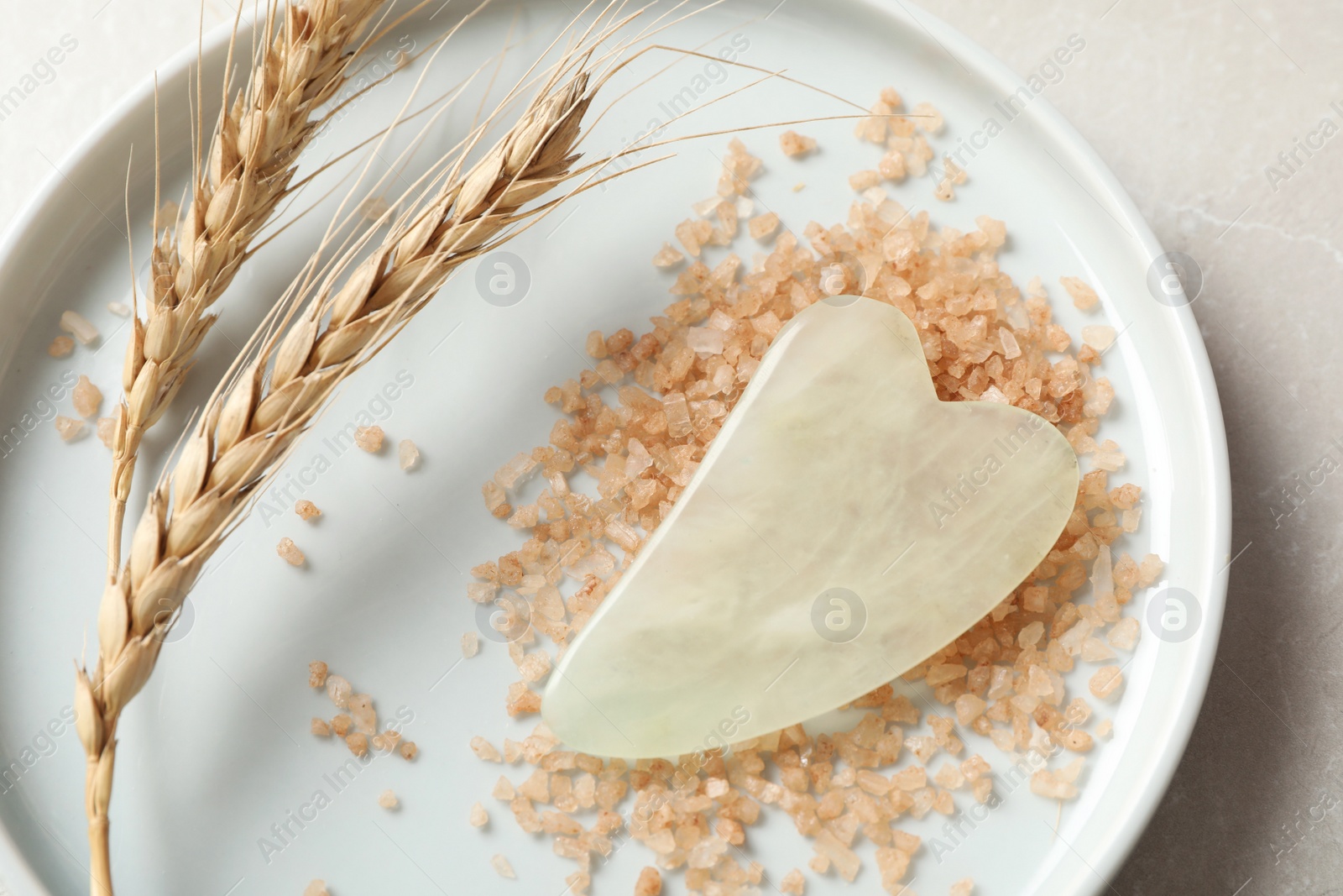 Photo of Jade gua sha tool, sea salt and spikes on grey table, above view