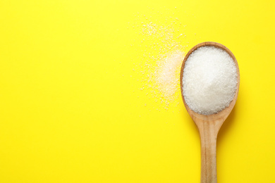 Granulated sugar in spoon on yellow background,top view. Space for text