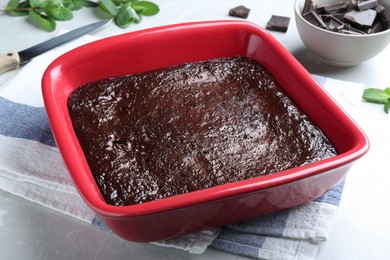 Delicious chocolate brownie in baking dish on light grey table