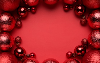 Frame of Christmas balls on red background, flat lay. Space for text