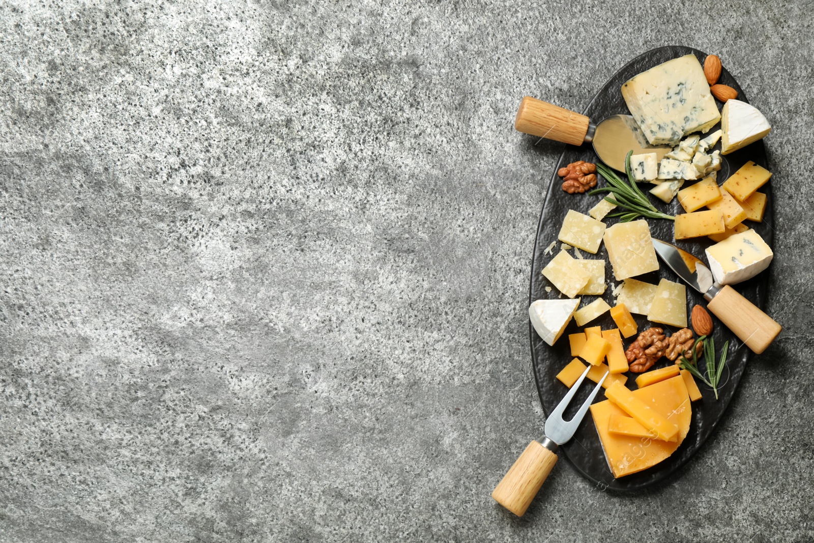 Photo of Cheese platter with specialized knives and fork on grey table, top view. Space for text