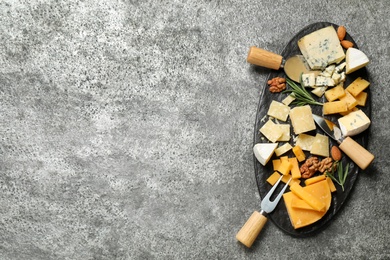 Photo of Cheese platter with specialized knives and fork on grey table, top view. Space for text