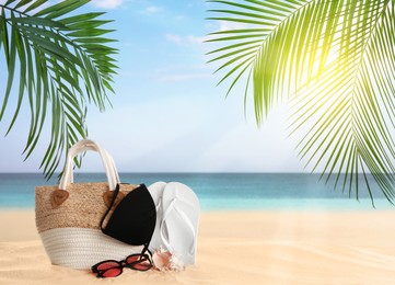 Image of Bag with bikini and accessories on sunny ocean beach, space for text. Summer vacation