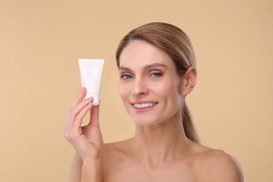 Woman holding tube of foundation on beige background