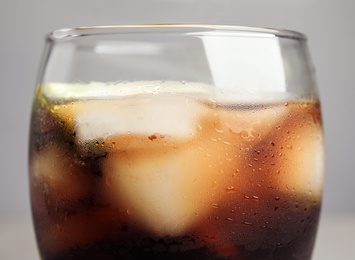 Photo of Glass of refreshing soda drink with ice cubes on grey background, closeup