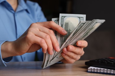 Photo of Money exchange. Woman counting dollar banknotes at wooden table, closeup