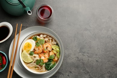 Delicious ramen with shrimps in bowl served on grey table, flat lay with space for text. Noodle soup