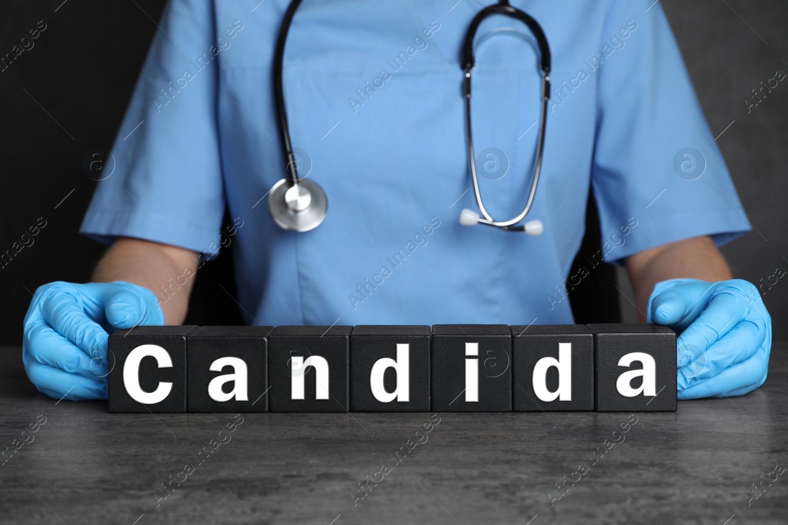 Image of Doctor holding black cubes with word Candida at grey table, closeup