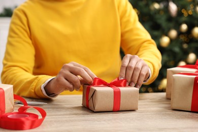 Man decorating Christmas gift box at wooden table indoors, closeup