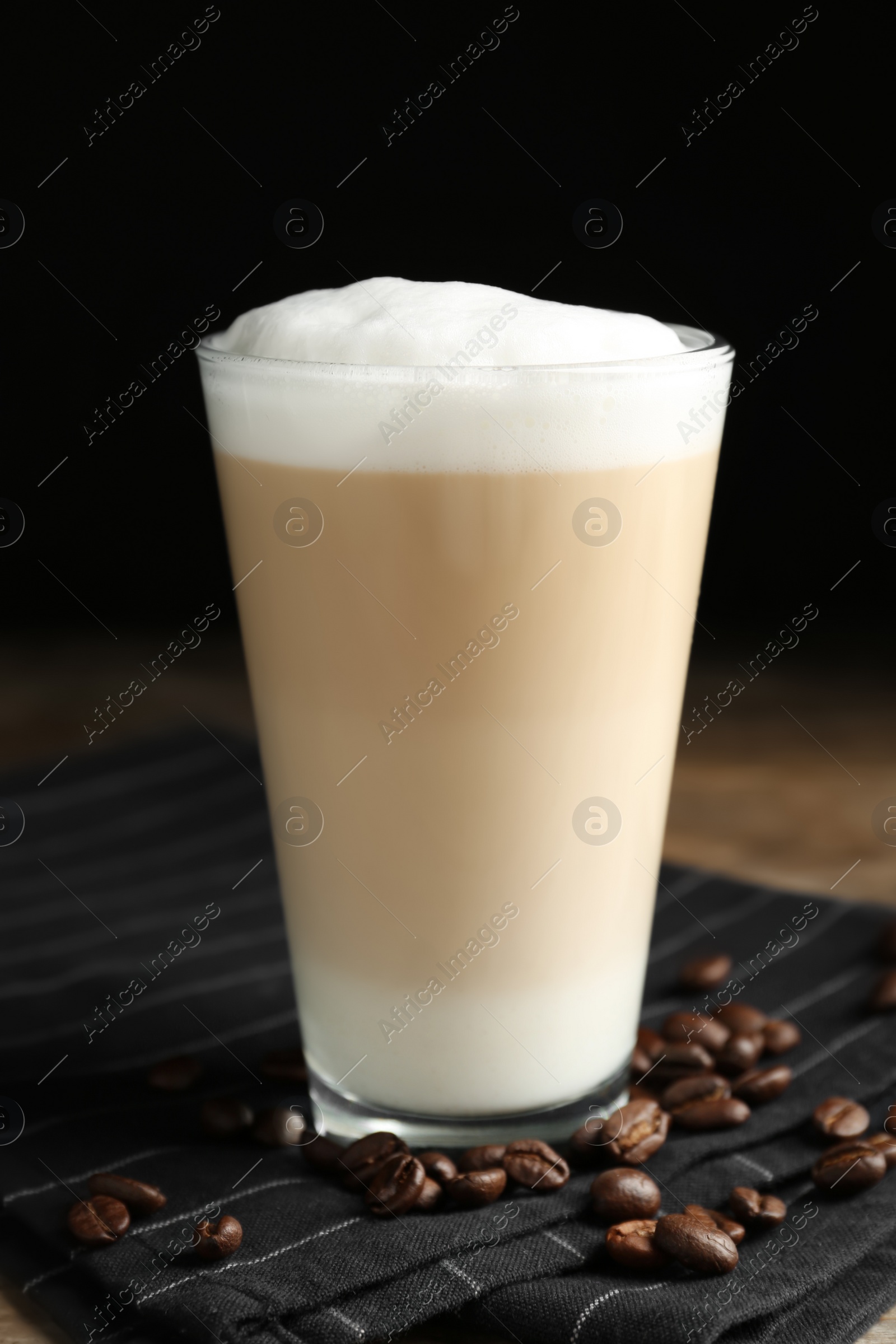 Photo of Delicious latte macchiato and coffee beans on napkin