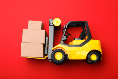 Photo of Top view of toy forklift with boxes on red background. Logistics and wholesale concept