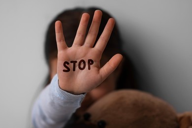 Image of No child abuse. Little girl showing hand with written Stop on palm, selective focus