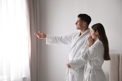 Happy couple wearing bathrobes near window in room