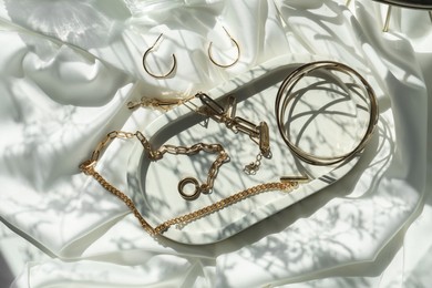 Photo of Metal chains and other different accessories on white fabric, flat lay. Luxury jewelry