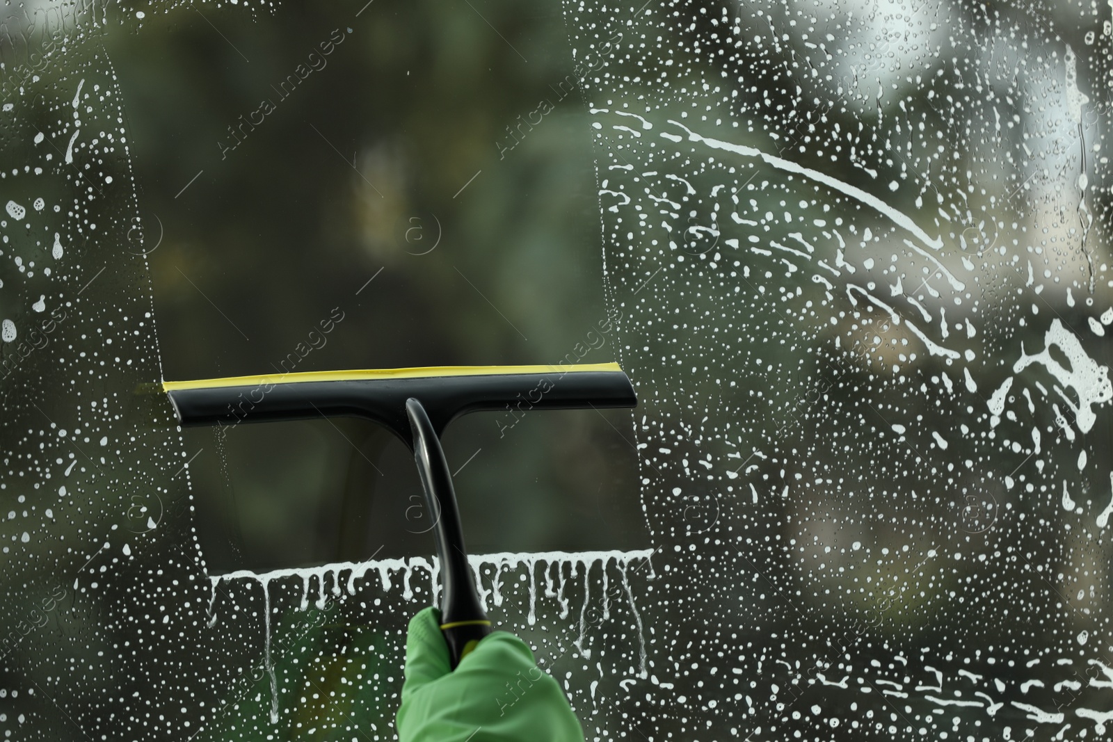 Photo of Woman cleaning glass with squeegee indoors, closeup