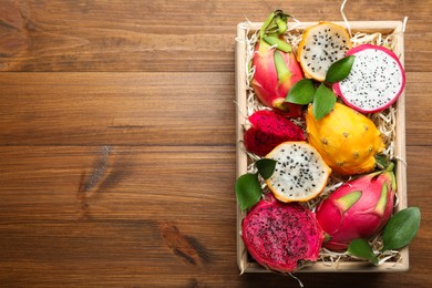Photo of Delicious cut and whole dragon fruits in crate on wooden table, top view. Space for text