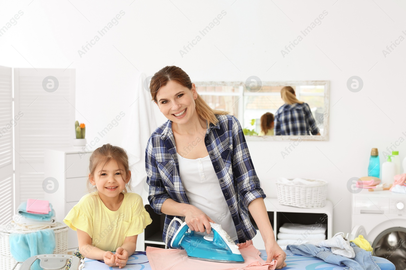 Photo of Housewife with daughter ironing clothes in laundry room