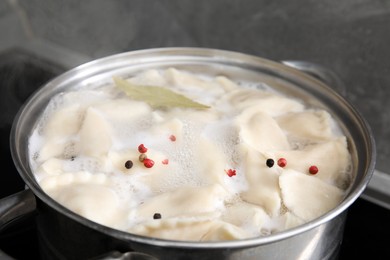 Photo of Cooking dumplings (varenyky) with tasty filling, peppercorns and bay leaf in pot indoors, closeup