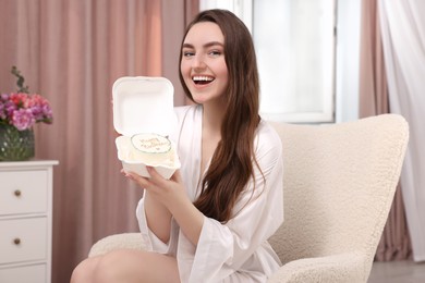 Photo of Beautiful young woman holding her Birthday cake on armchair in room