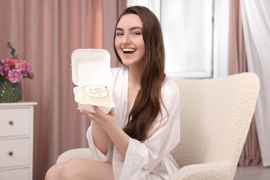 Beautiful young woman holding her Birthday cake on armchair in room