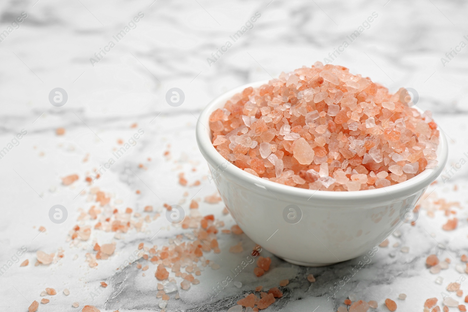 Photo of Bowl and pink himalayan salt on white marble table, closeup. Space for text