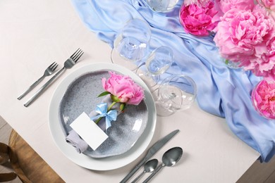 Stylish table setting with beautiful peonies, napkin and blank card, above view