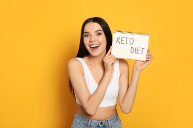 Photo of Emotional woman holding notebook with words Keto Diet on yellow background