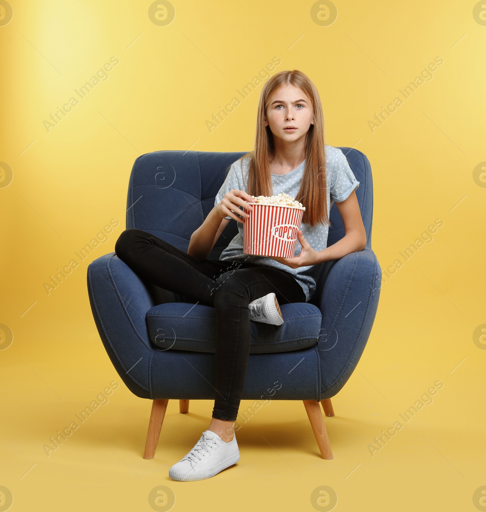 Photo of Emotional teenage girl with popcorn sitting in armchair during cinema show on color background