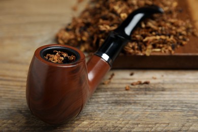 Photo of Smoking pipe with dry tobacco on wooden table, closeup