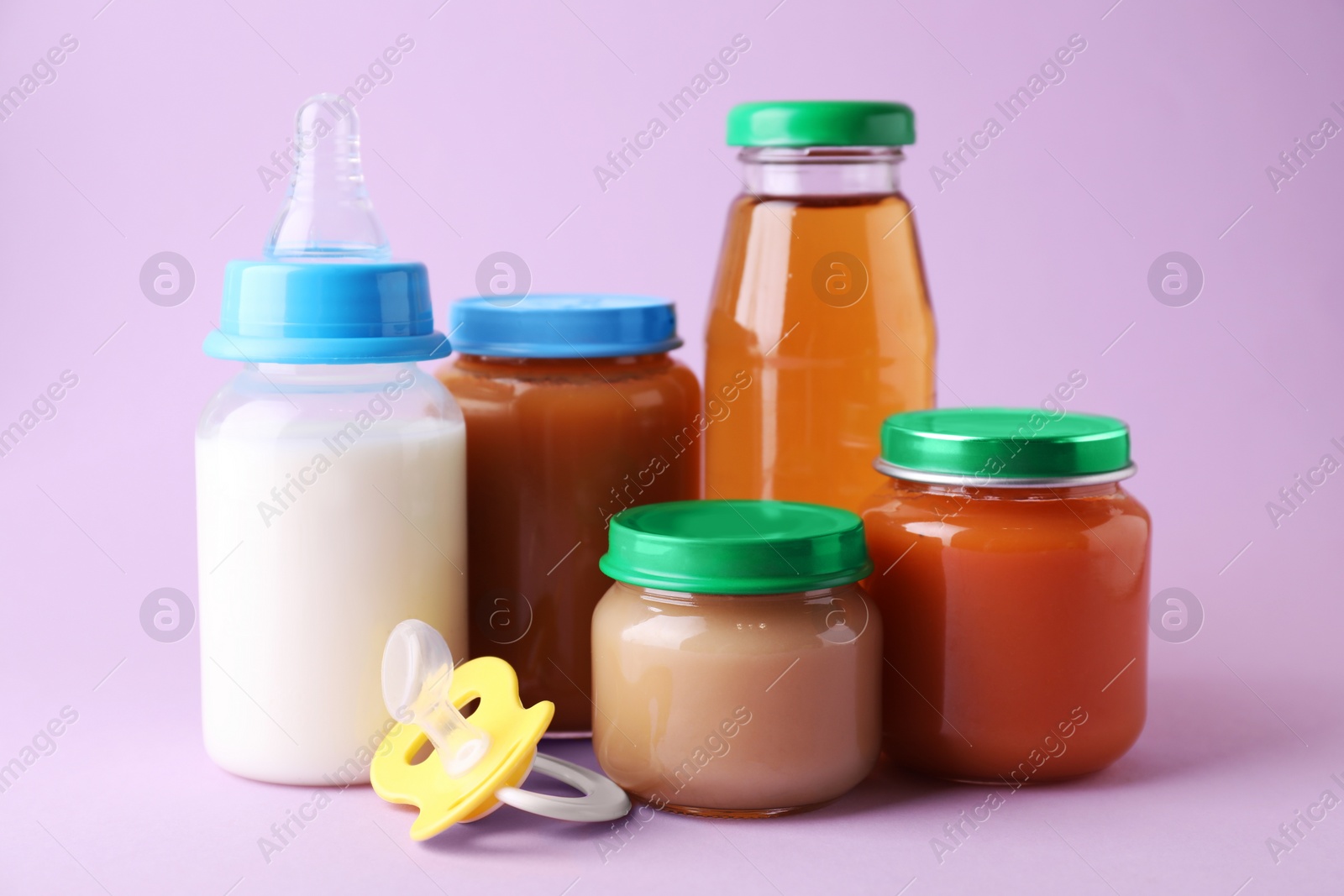 Photo of Healthy baby food, juice, milk and pacifier on lilac background