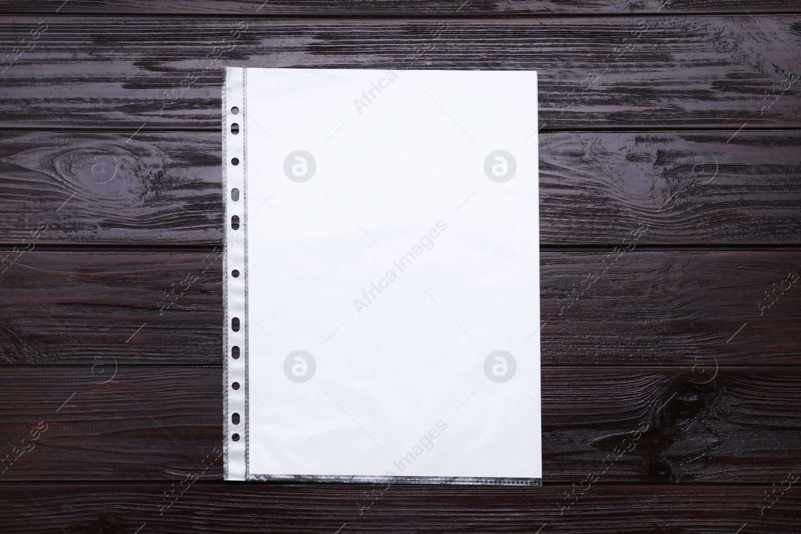 Photo of Punched pocket with paper sheet on brown wooden table, top view. Space for text