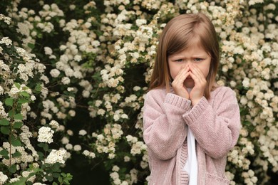 Little girl suffering from seasonal pollen allergy near blossoming tree on spring day