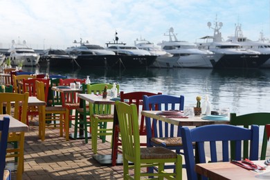 Beautiful view of outdoor cafe with colorful wooden chairs near pier