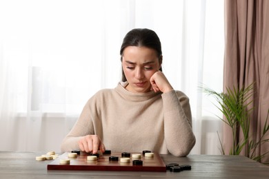 Photo of Playing checkers. Concentrated woman thinking about next move at table in room