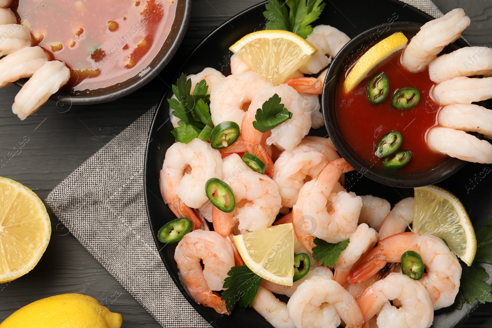 Photo of Tasty boiled shrimps with cocktail sauce, chili, parsley and lemon on grey wooden table, flat lay