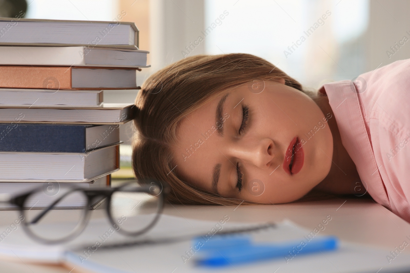 Photo of Young tired woman sleeping near books at white table indoors, closeup