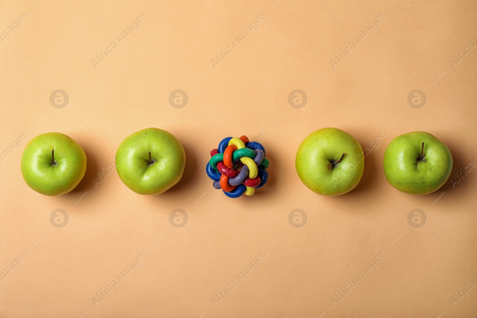 Photo of Row of apples with toy ball on color background. Be different