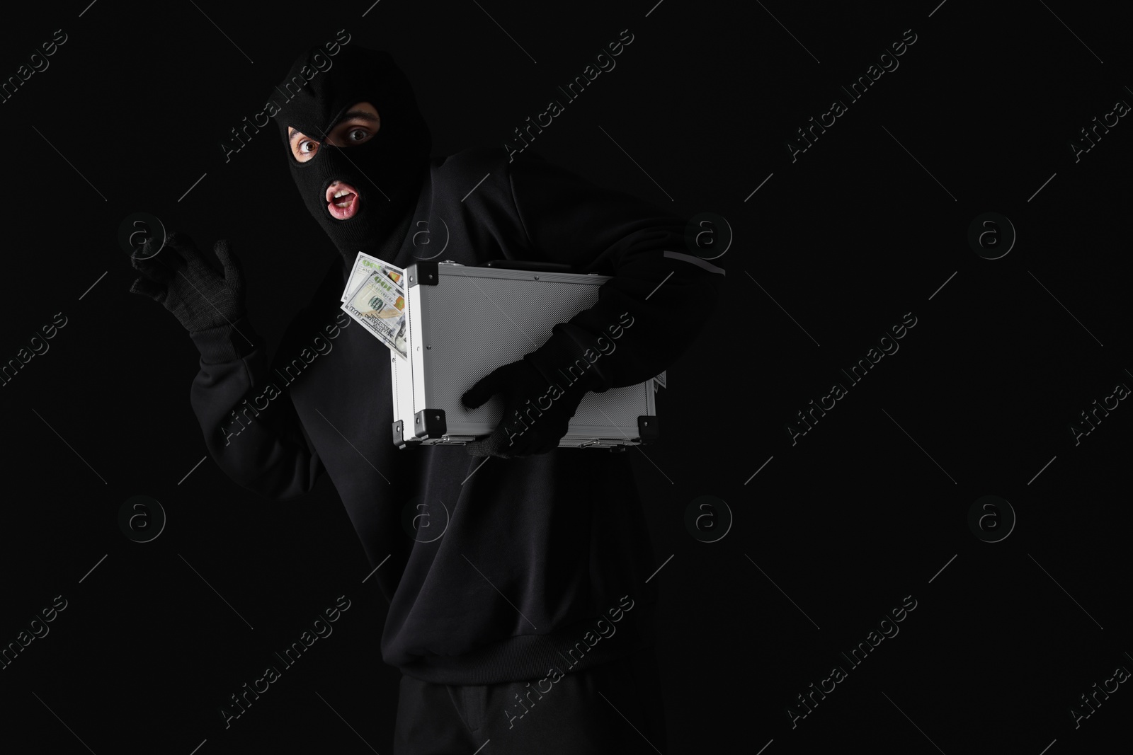 Photo of Thief in balaclava with briefcase of money on black background. Space for text