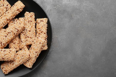 Plate with tasty sesame seed bars on grey table, top view. Space for text