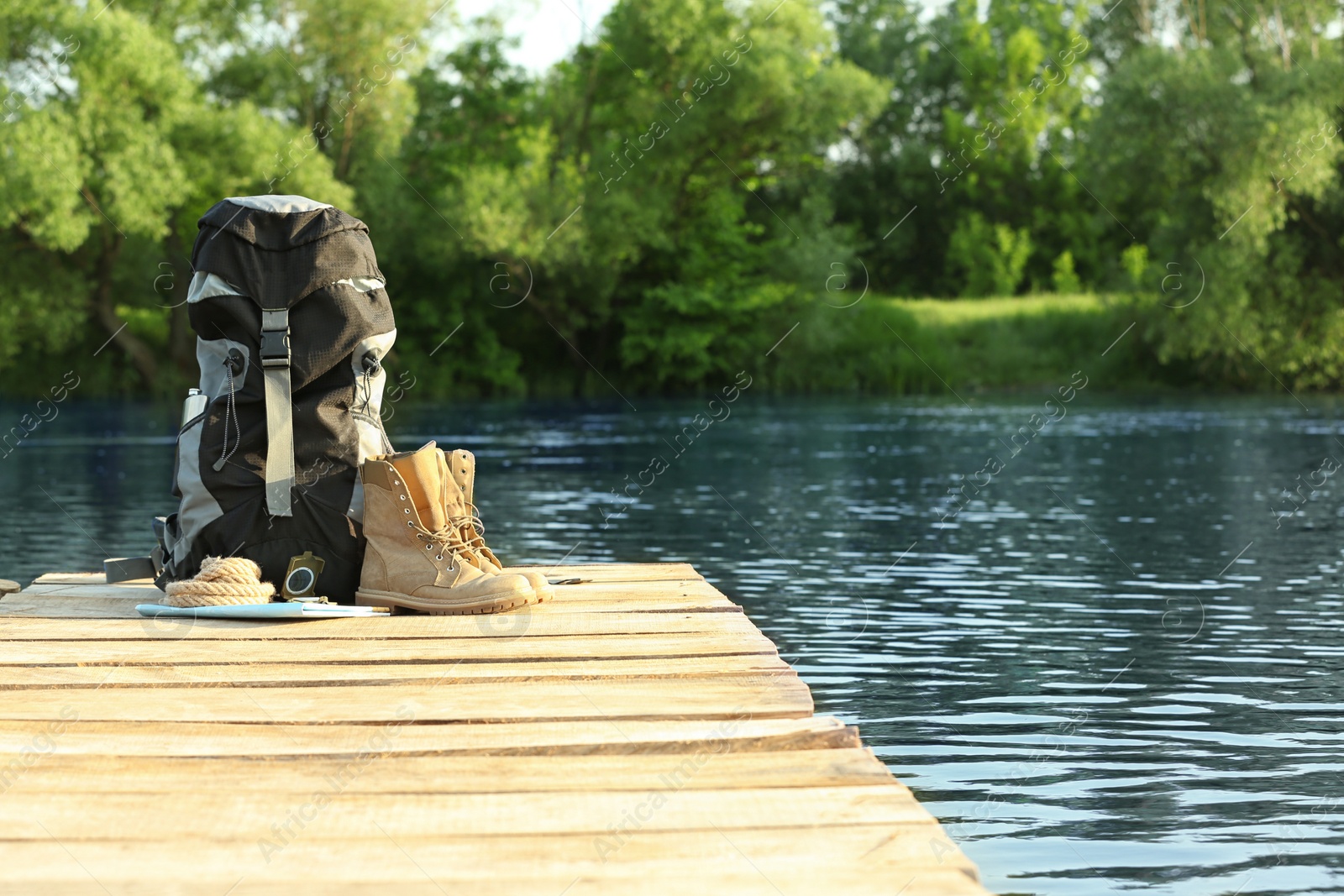 Photo of Backpack and camping equipment on wooden pier near river. Space for text