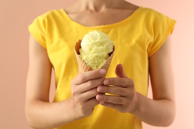 Photo of Woman holding yellow ice cream in wafer cone on pink background, closeup