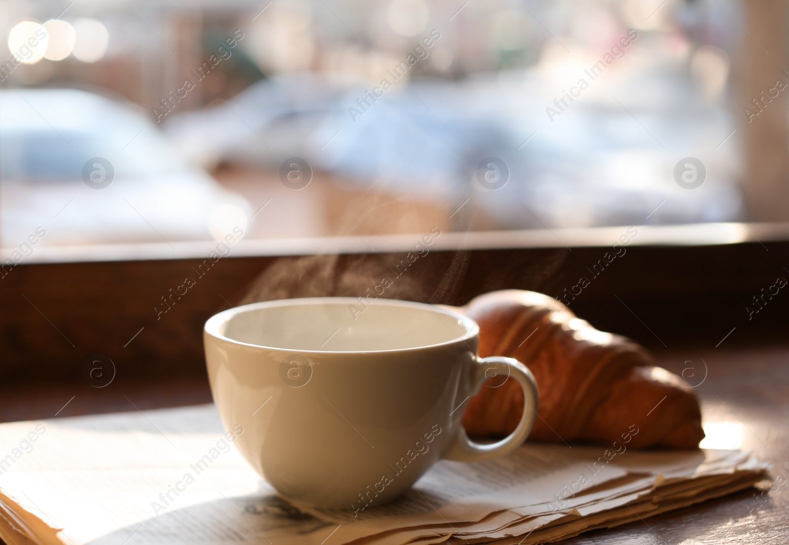 Photo of Delicious morning coffee, newspaper and croissant near window, indoors