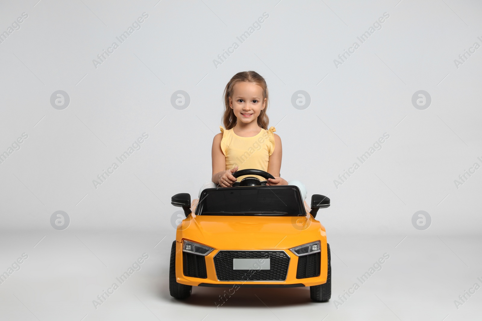 Photo of Cute little girl driving children's electric toy car on grey background