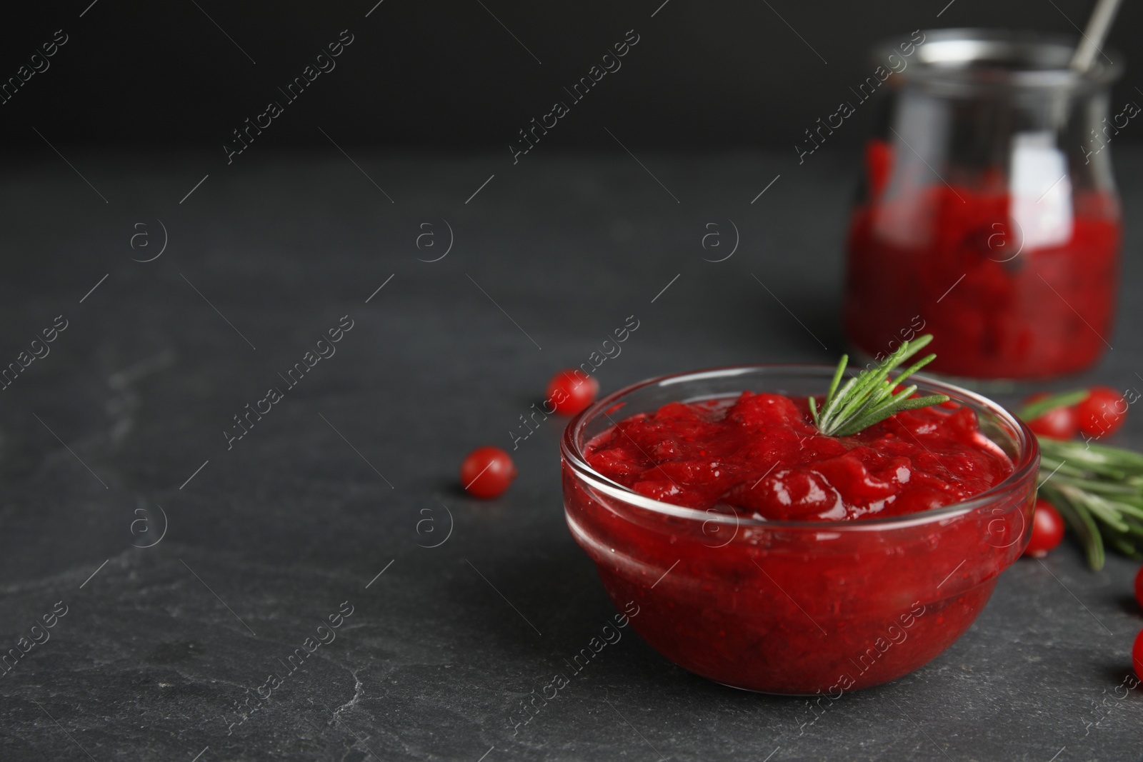 Photo of Bowl of cranberry sauce with rosemary on grey table, closeup. Space for text