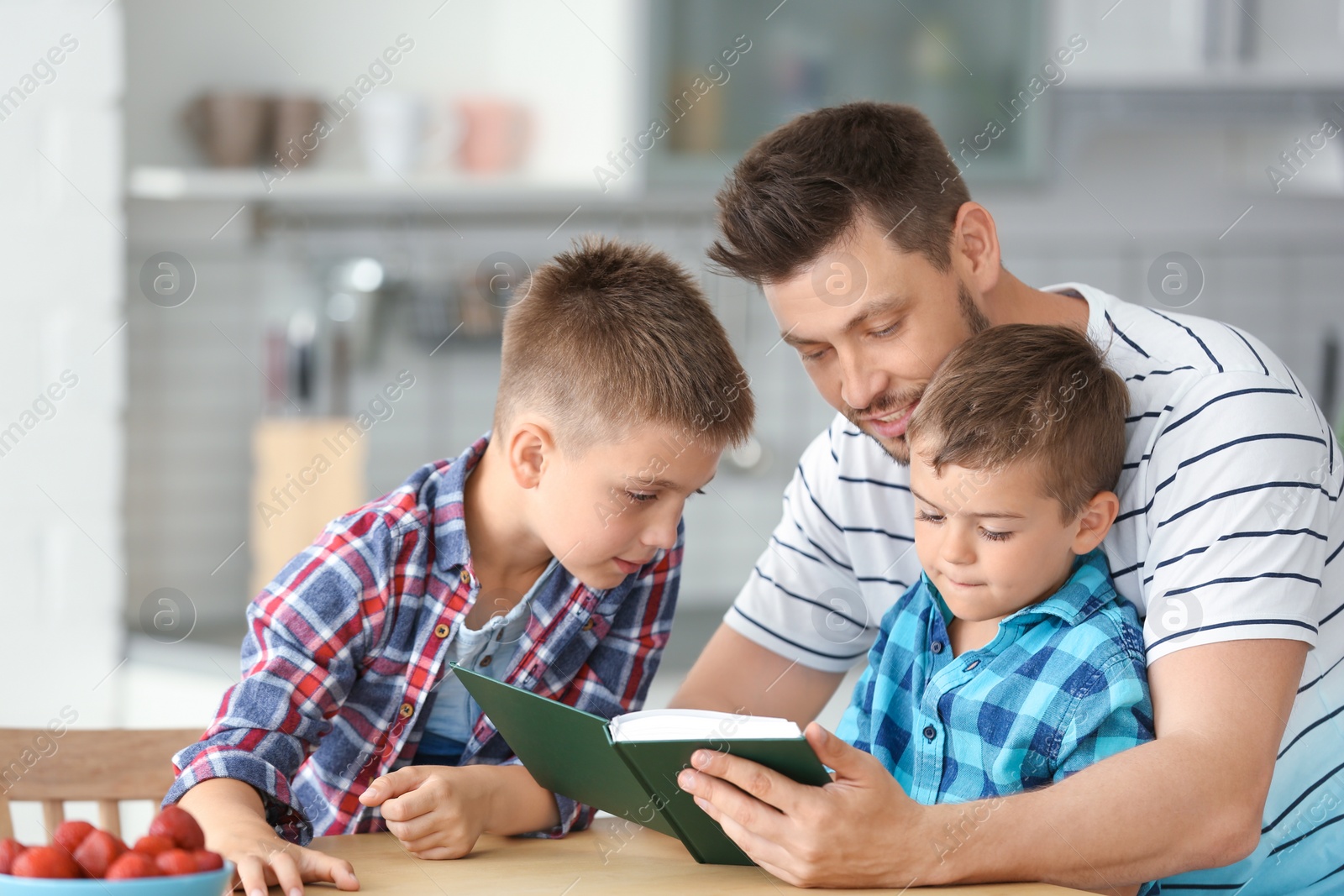 Photo of Dad and his sons reading interesting book in kitchen