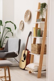 Photo of Spring atmosphere. Wooden shelving unit, acoustic guitar and comfortable chair in stylish room