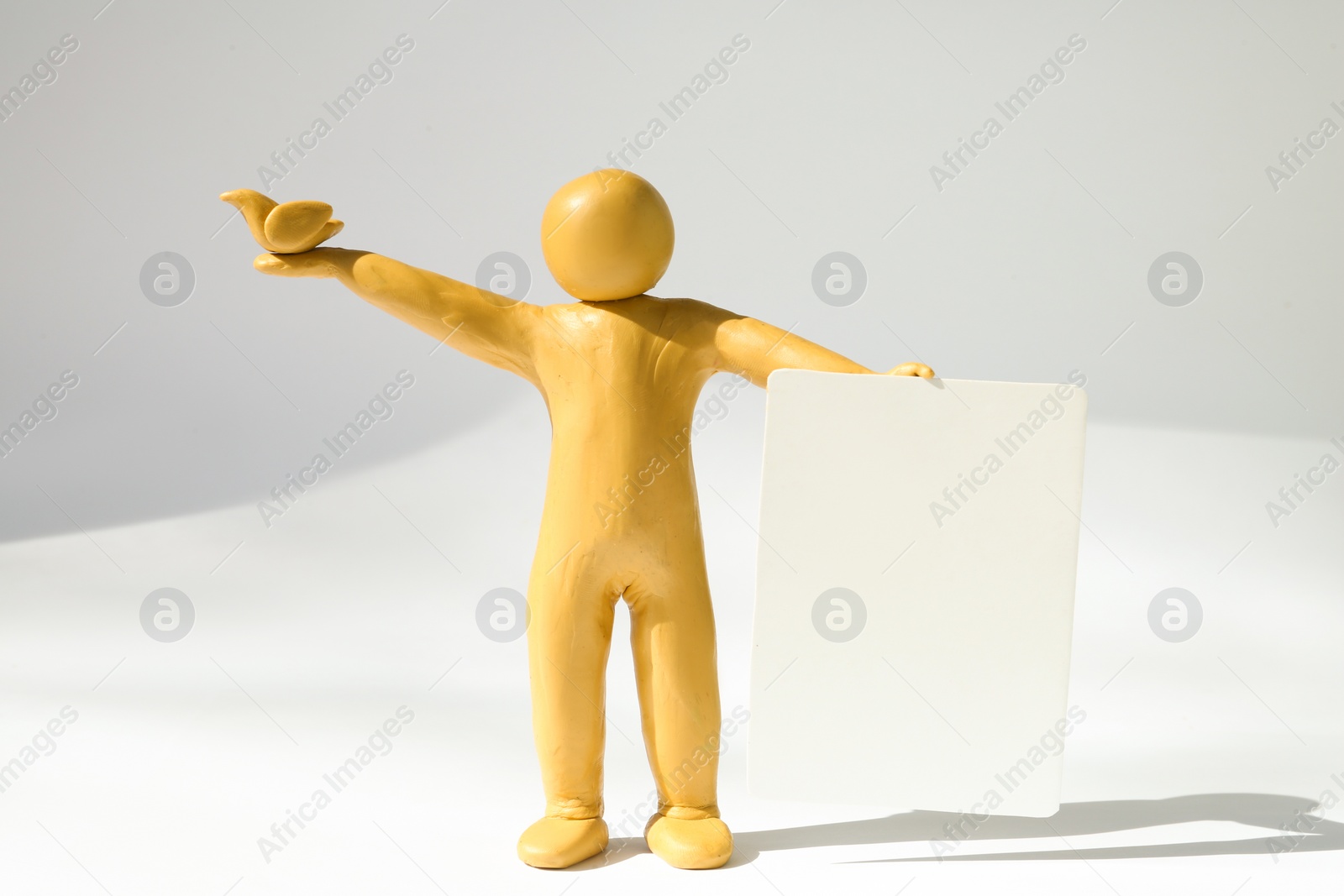 Photo of Yellow plasticine human figure with dove and blank card on white background, space for text